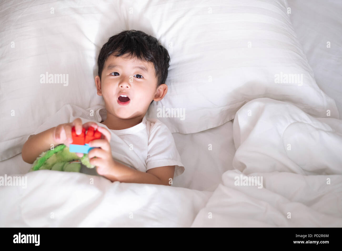 3 years old little cute Asian boy in white shirt at home on the bed, kid lying playing and