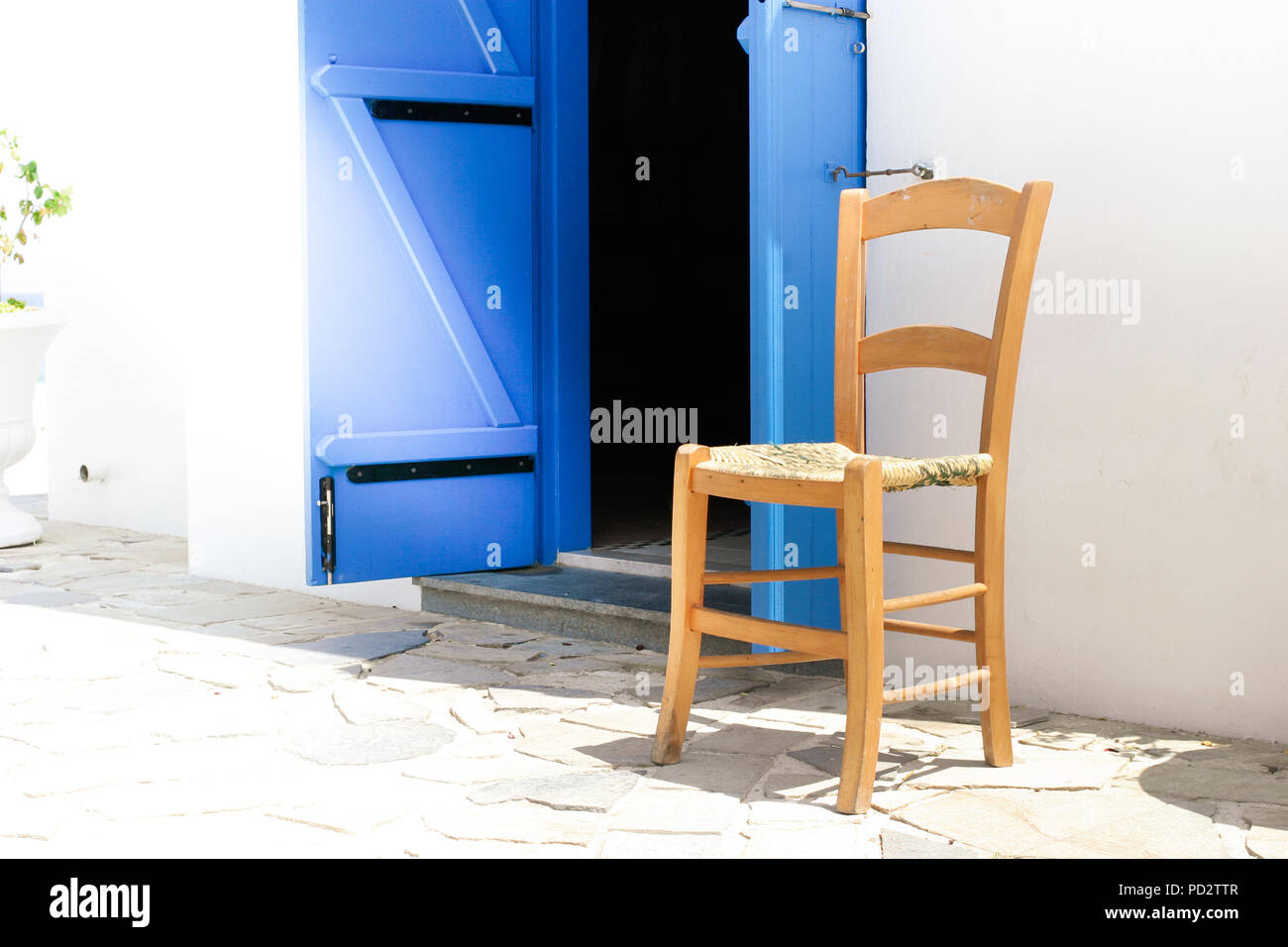 Isolated chair outside a church, with a blue door opening. Sun is shining into the doorway. Stock Photo