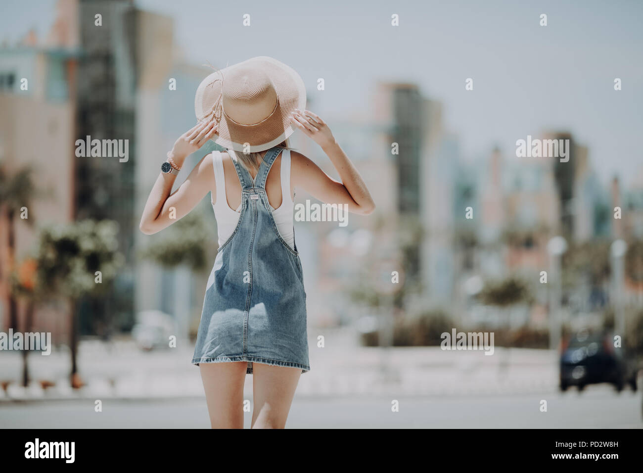 Rear view of young woman walking on city street wearing hat enjoying ...