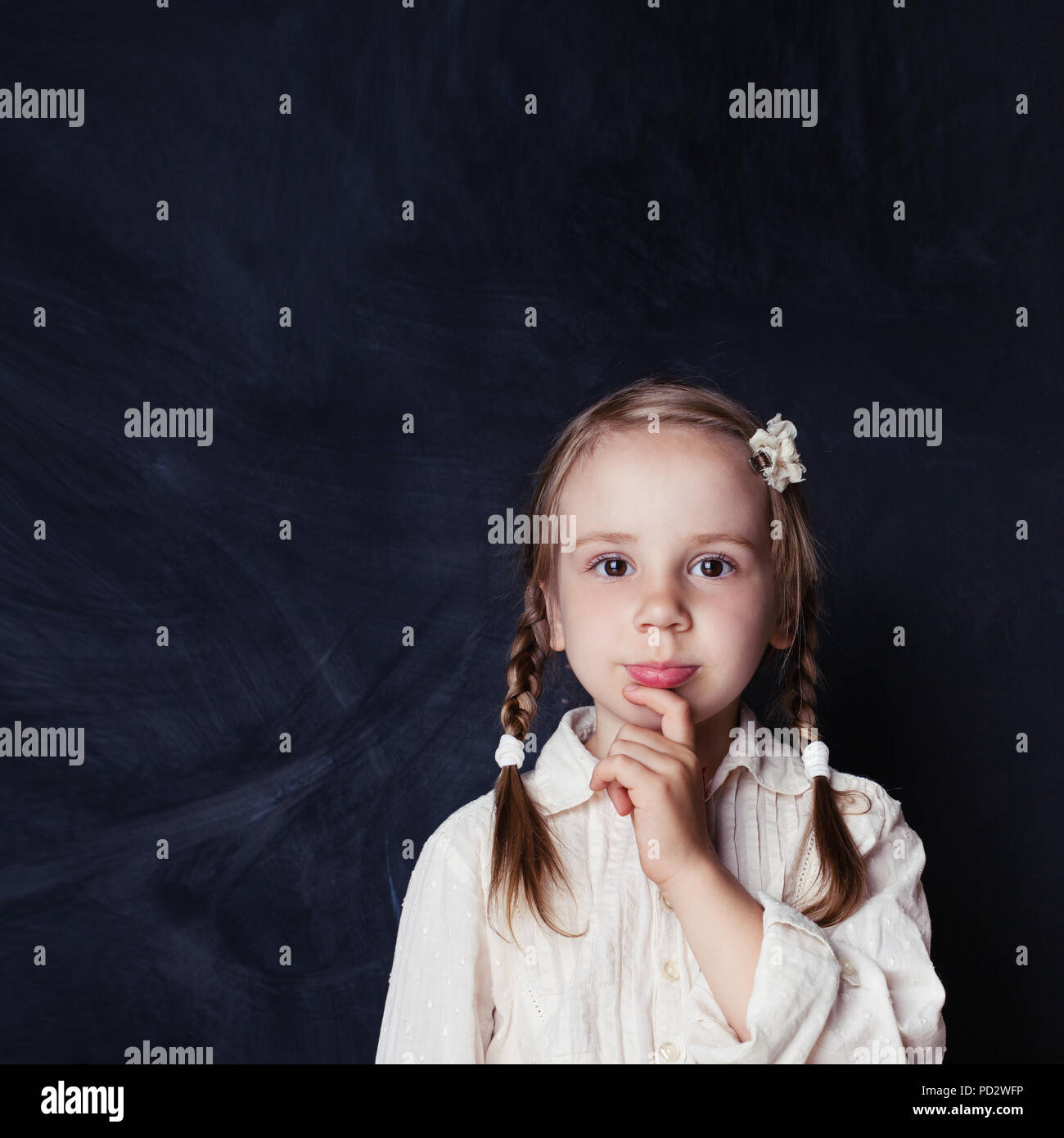 Сurious child thinking. Little girl on chalk board background with copy space. Back to school, kid creativity and brainstorming concept Stock Photo