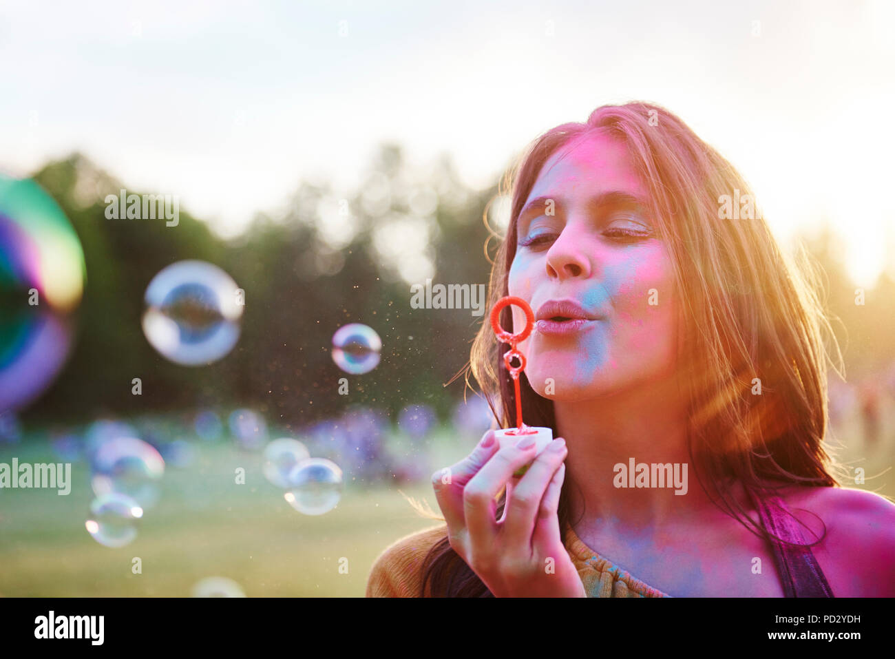 Young woman covered in coloured chalk powder blowing bubbles at Holi Festival Stock Photo