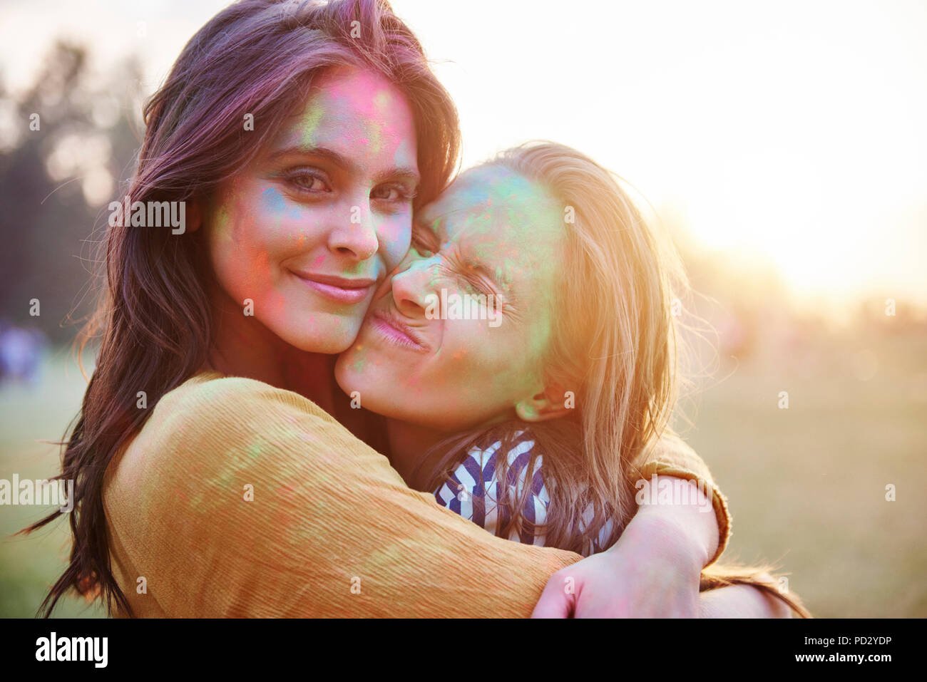 Two young women with faces covered in coloured chalk powder hugging at Holi Festival, portrait Stock Photo