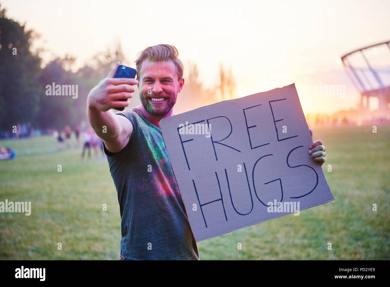Young man taking selfie holding free hugs sign at Holi Festival Stock Photo