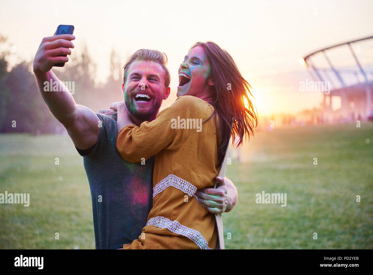 Young couple covered in coloured chalk powder taking selfie at Holi Festival Stock Photo