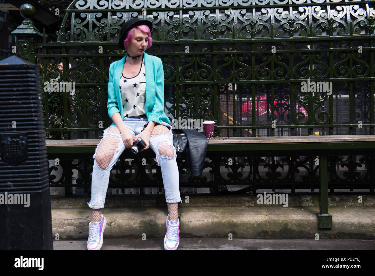 Young woman with pink hair and quirky style sitting on bench, London, UK Stock Photo