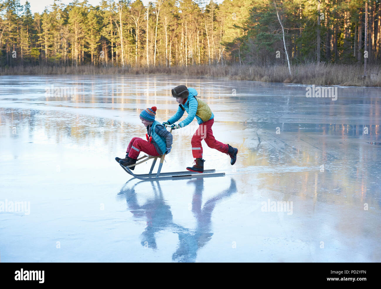 Boy pushing his brother on sleigh across frozen lake Stock Photo