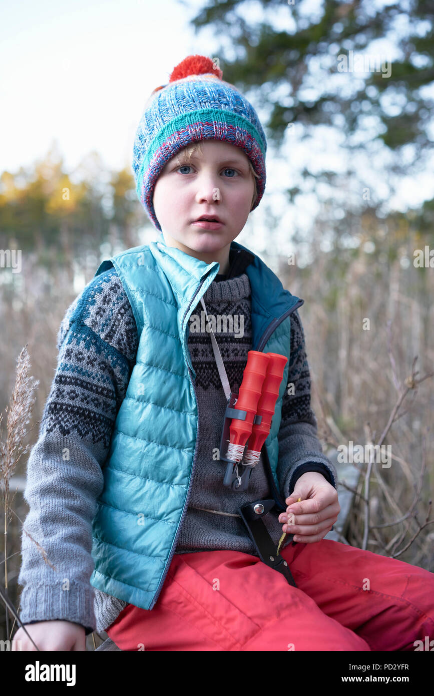 Boy in knitted hat sitting on bench in reeds, portrait Stock Photo