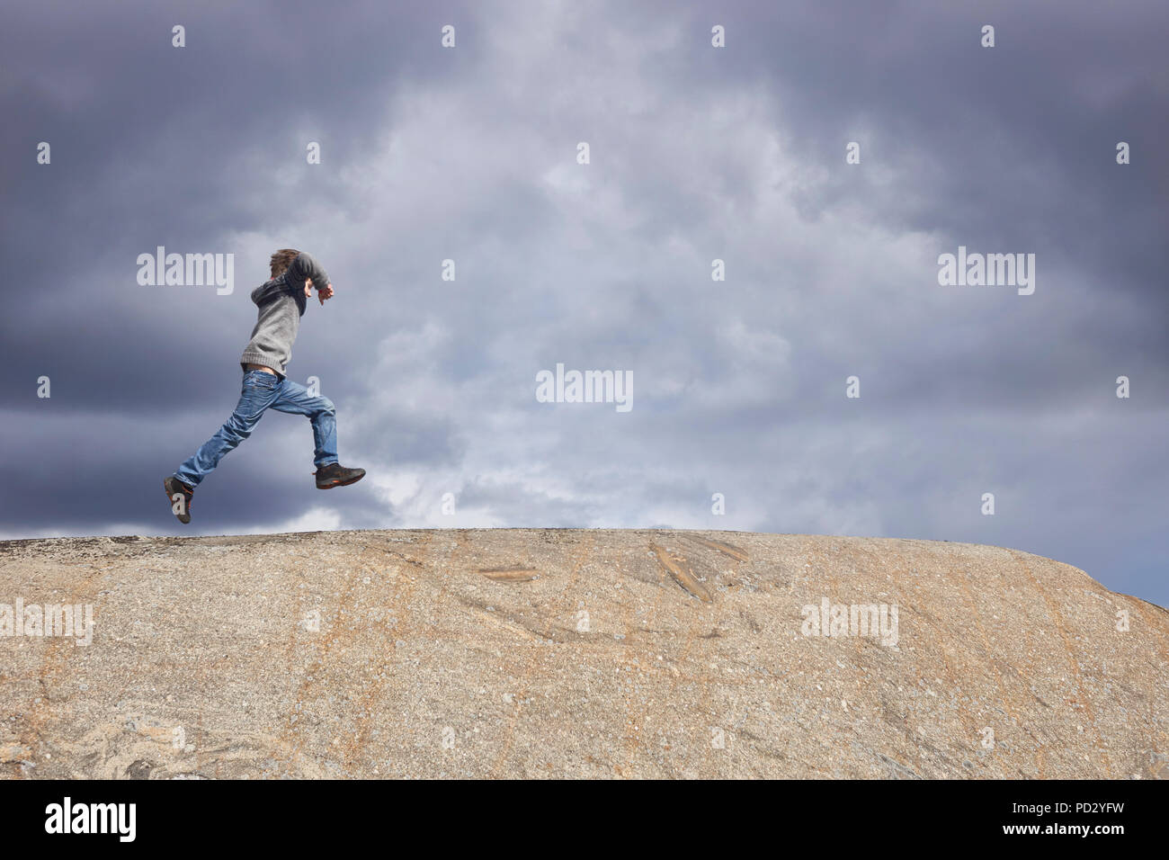 Boy running on top of rock against stormy cloud sky Stock Photo