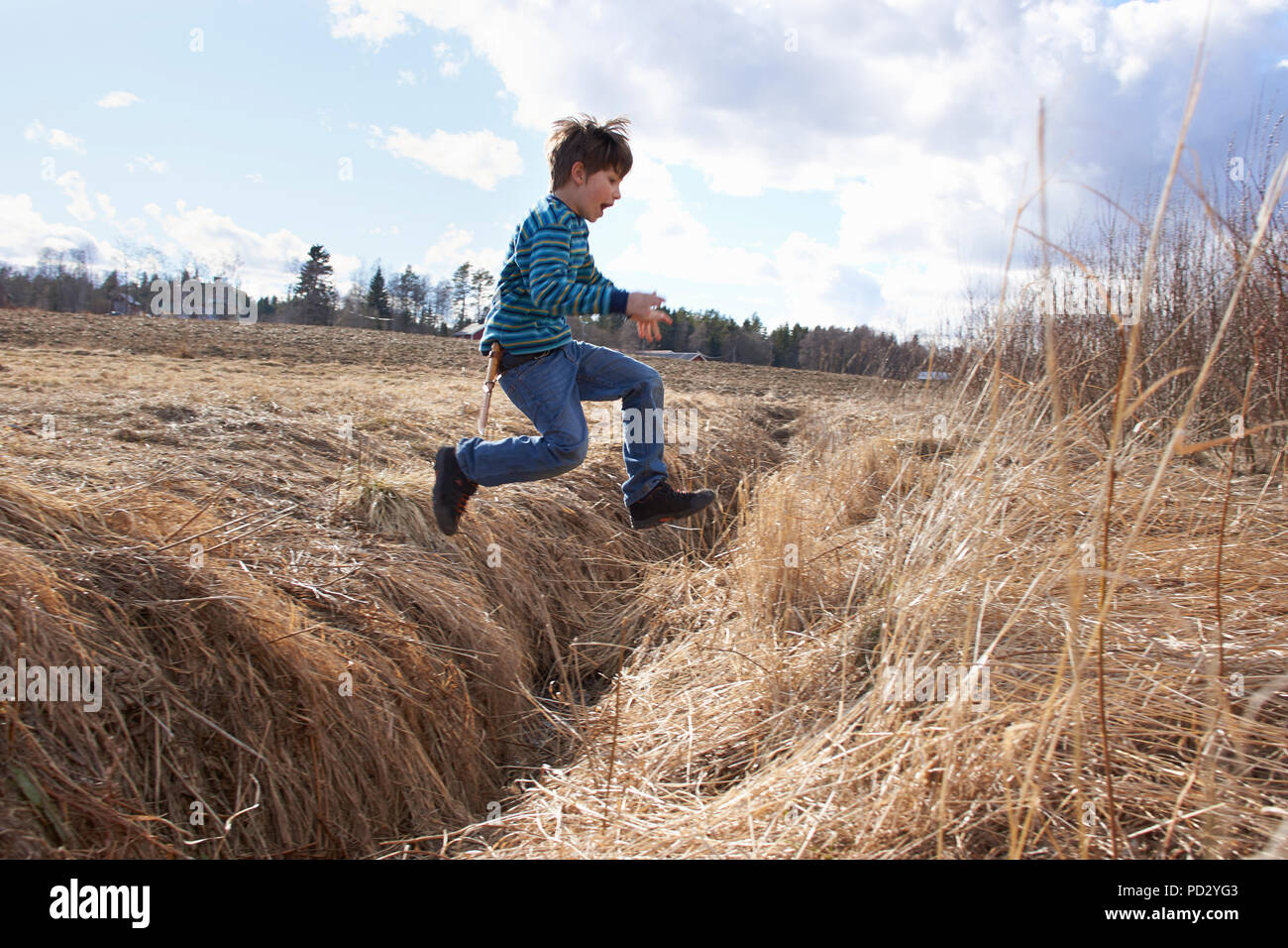 Boy jumping across field ditch Stock Photo