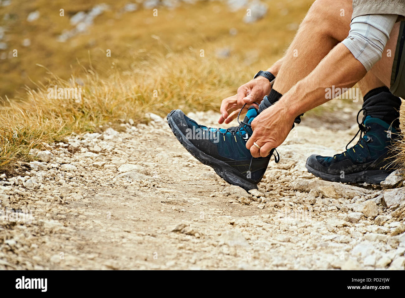 Hiker tying laces on dirt track, Canazei, Trentino-Alto Adige, Italy Stock Photo