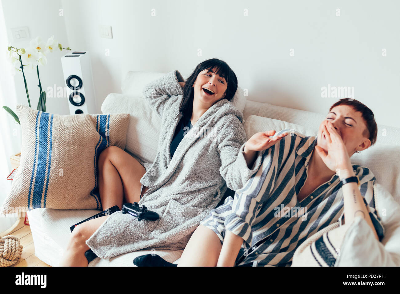 Women in nightwear relaxing on sofa, laughing Stock Photo
