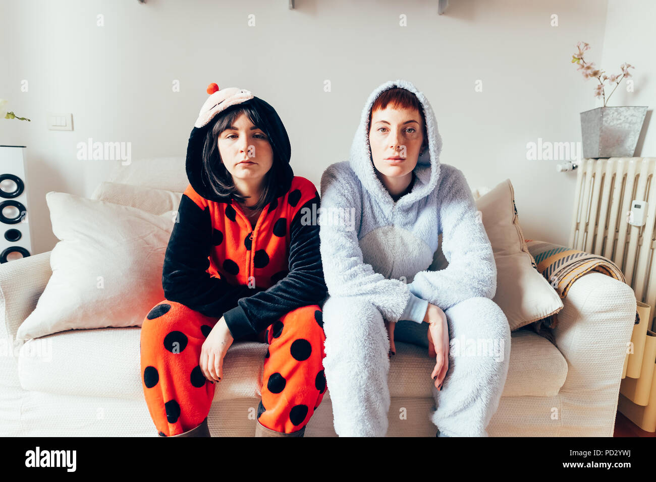 Portrait of women sitting on sofa wearing adult bodysuits looking at camera Stock Photo
