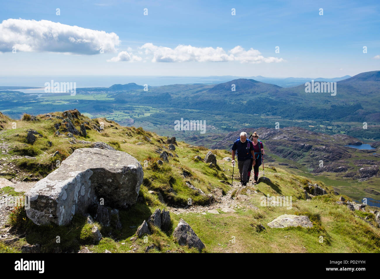 Two hikers hiking on path near Cnicht mountain top in Snowdonia National Park with scenic view to coast in summer.  Croesor Gwynedd Wales UK Britain Stock Photo