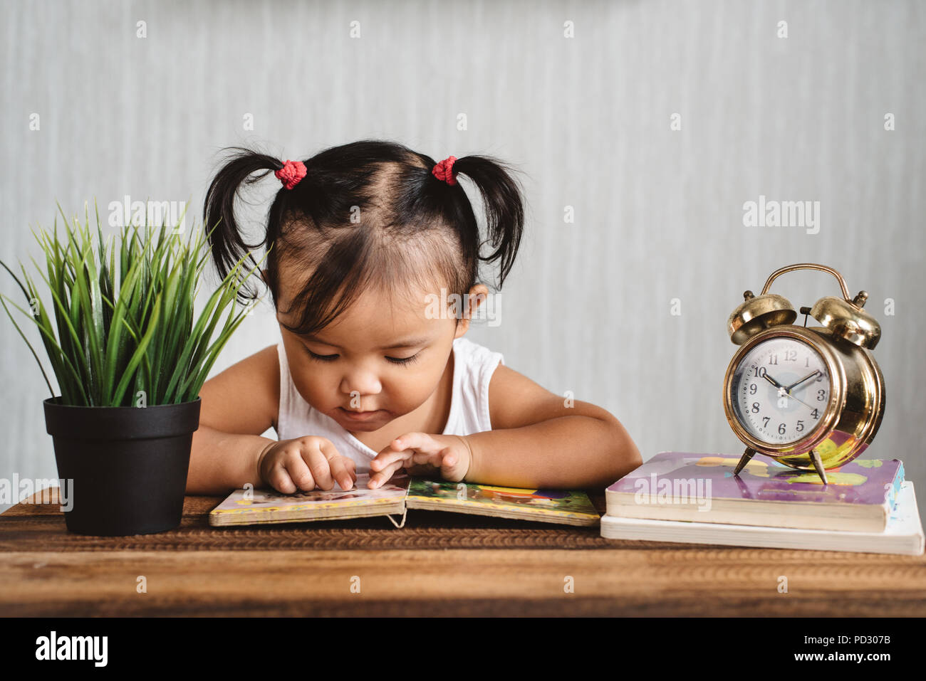 asian baby toddler reading a book on wooden table. concept of early education, child learning, development,  growth and parenting Stock Photo