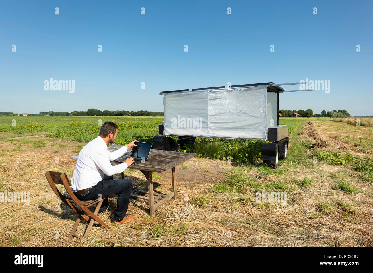 Man checking on robot monitoring crops and flowers on agricultural site in pixelfarming research Stock Photo