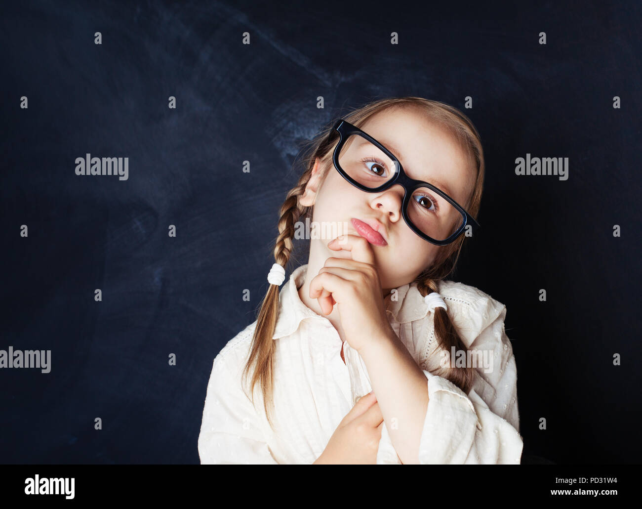 Little girl in glasses thinking on blue background with copy space. Back to school, Kid Creativity and Education Concept Stock Photo