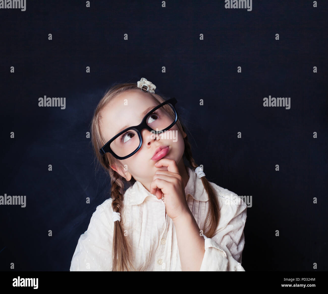 Сurious little girl thinking on empty chalk board background with copy space. Child back to school, kid creativity and brainstorming concept Stock Photo