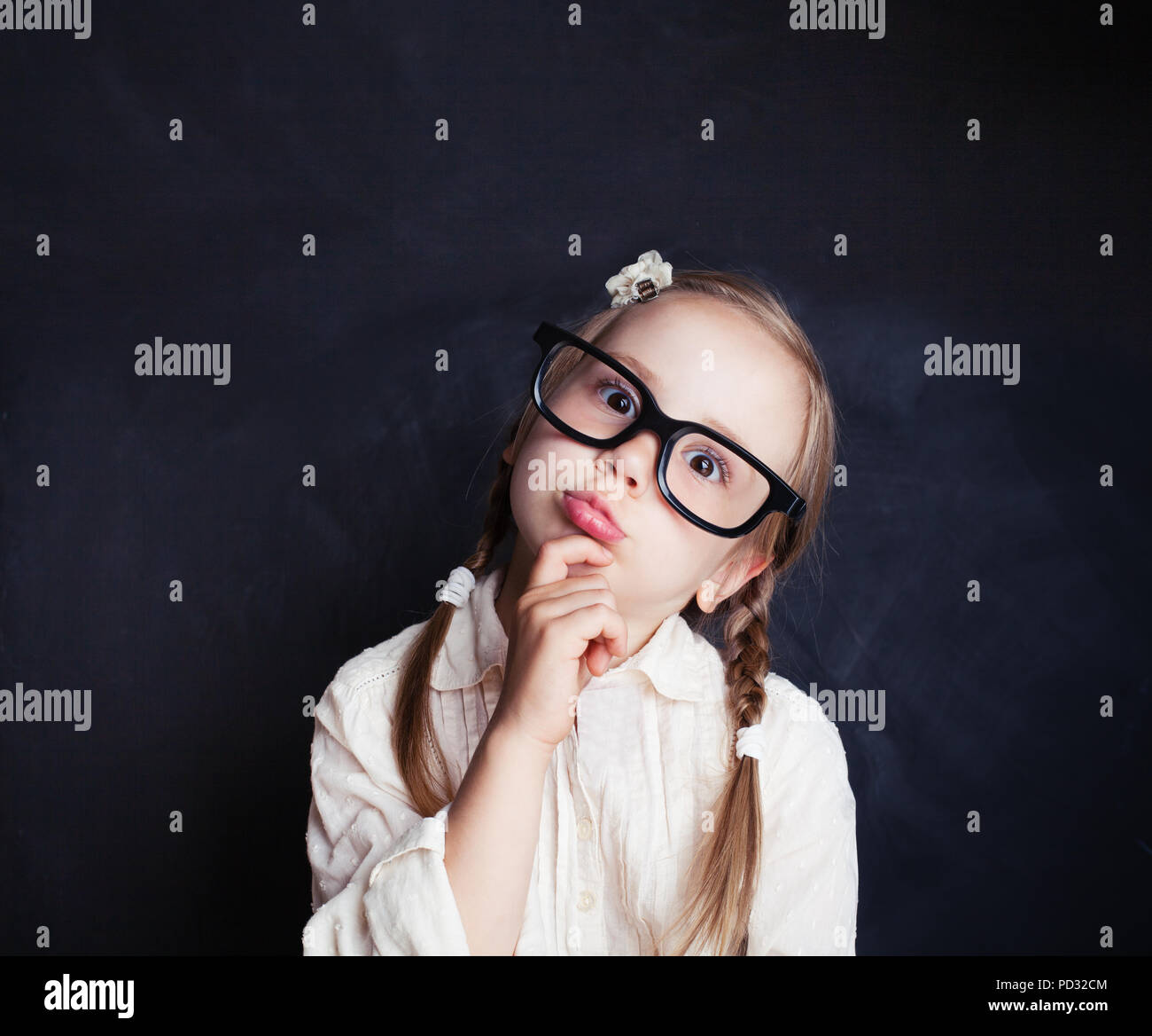 Сurious child thinking. Funny little girl in glasses on chalk board background with copy space. Back to school, kid creativity and brainstorming conce Stock Photo