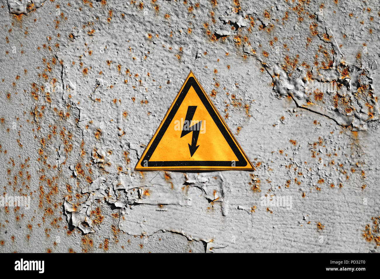 Yellow high voltage triangle warning sign on rusty gray metal wall Stock Photo