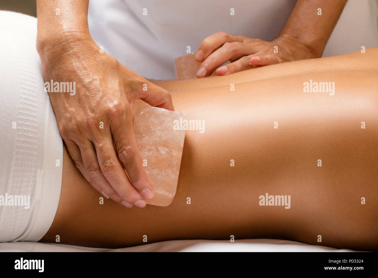 Close up detail of himalayan salt stone massage. Therapist massaging lower back of woman with hot salt brick. Stock Photo