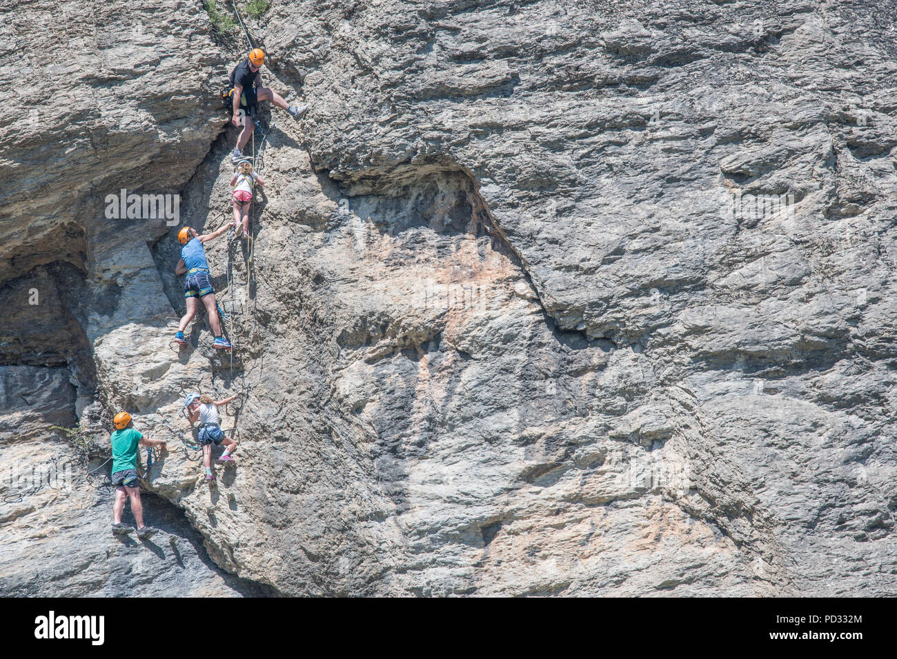 An english family on holiday at L'Argentierre la Bessee, France, climb the via ferrrata on the steep rocky cliff face to the clock tower. Stock Photo