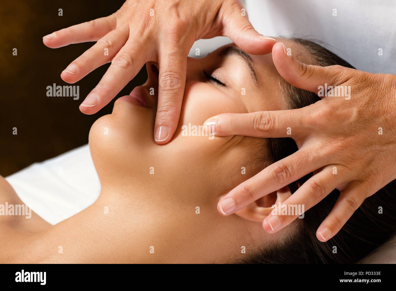Close up portrait of woman at beauty treatment in spa.Therapist massaging and stretching female cheek for product penetration. Stock Photo