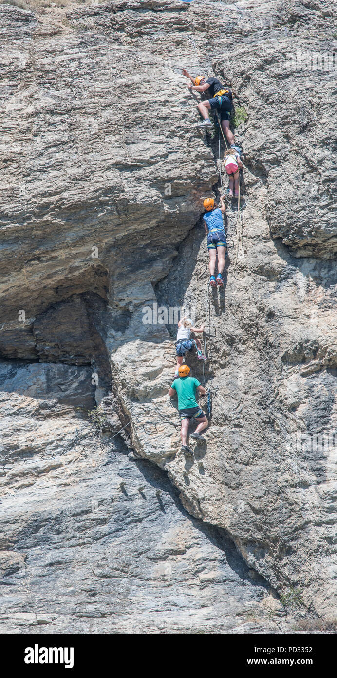 An english family on holiday at L'Argentierre la Bessee, France, climb the via ferrrata on the steep rocky cliff face to the clock tower. Stock Photo