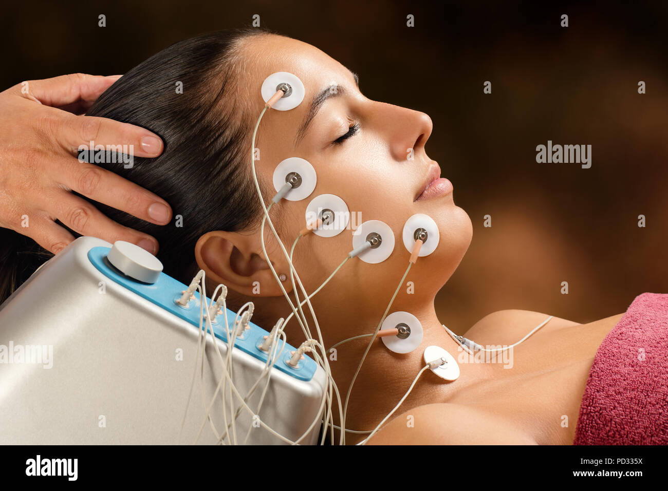 Close up portrait of woman having skin tightening treatment with low frequency electrodes. Hypo allergenic pads placed on woman’s face. Stock Photo