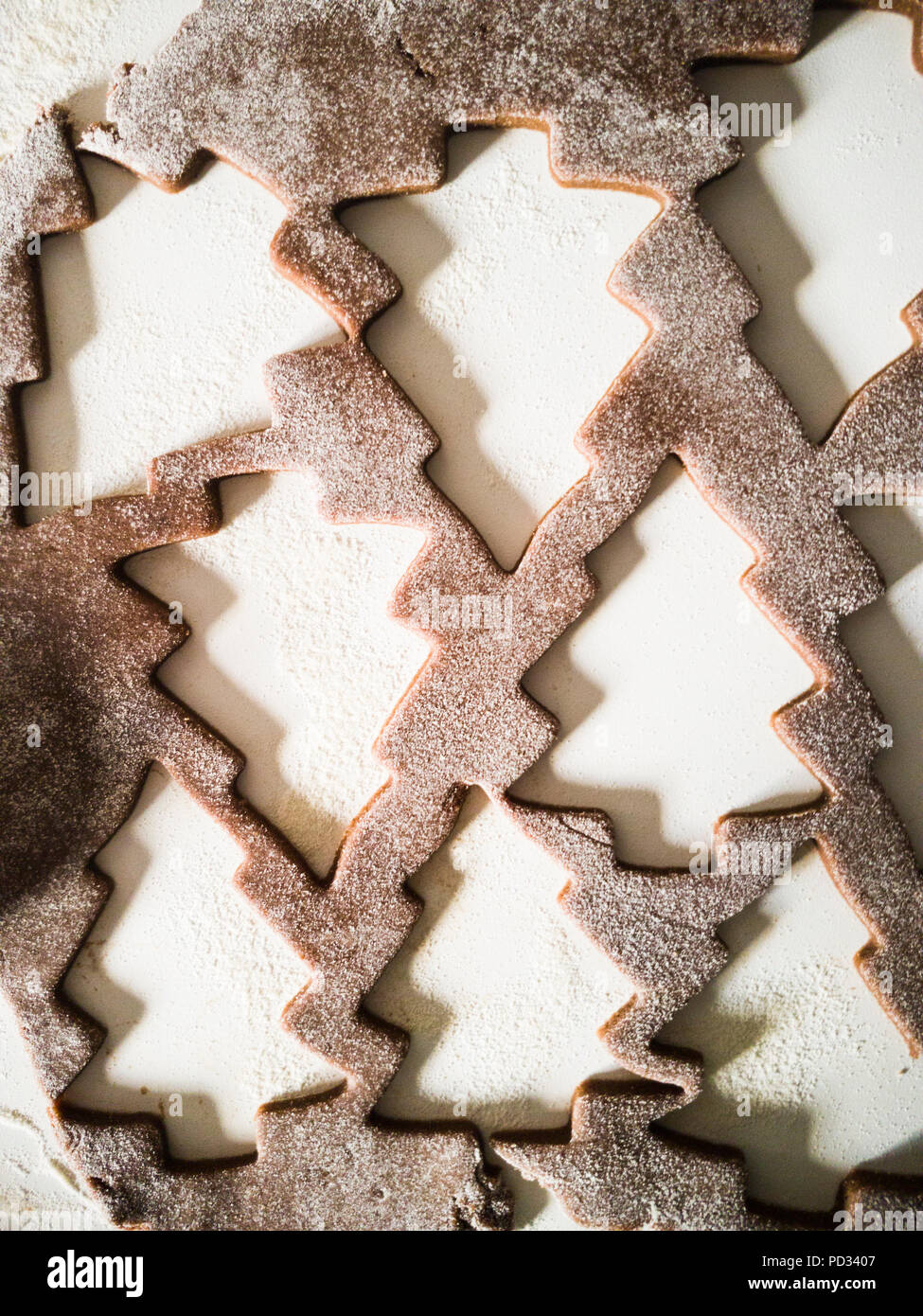 Close-up of raw pastry cutters with holes in a shape of Christmas trees, on a white background with flour around.  Raw gingerbread dough. Stock Photo