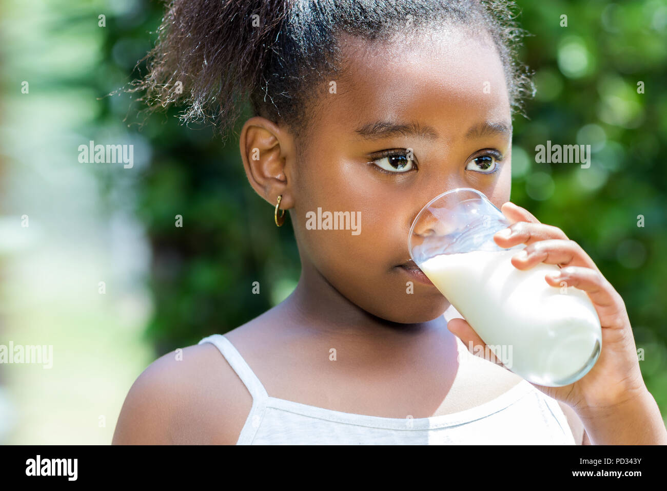 Close up portrait of cute little african girl drinking glass of milk in garden. Stock Photo
