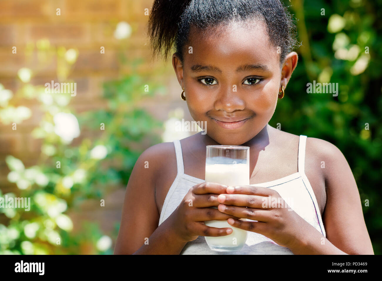 Close up portrait of cute little african girl holding glass with milk in garden. Stock Photo