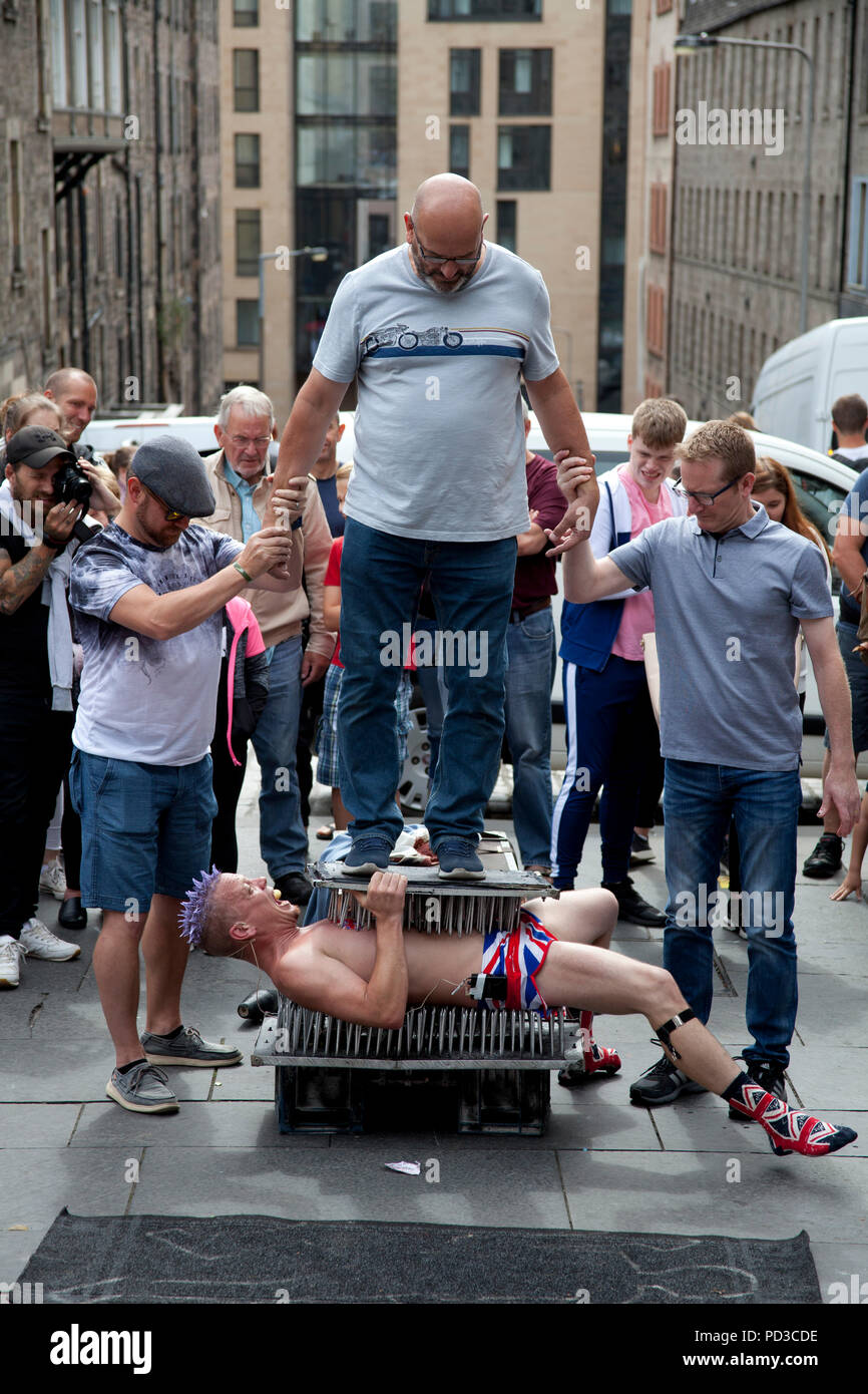 Edinburgh, Scotland, UK. 6 Aug. 2018, Edinburgh Fringe Festival street performer at Tron, on Royal Mile, performing on a bed of nails with union jack shorts. Stock Photo