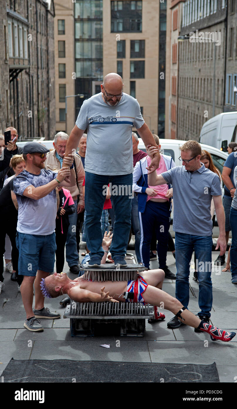 Edinburgh, Scotland, UK. 6 Aug. 2018, Edinburgh Fringe Festival street performer at Tron, on Royal Mile, performing on a bed of nails with union jack shorts. Stock Photo