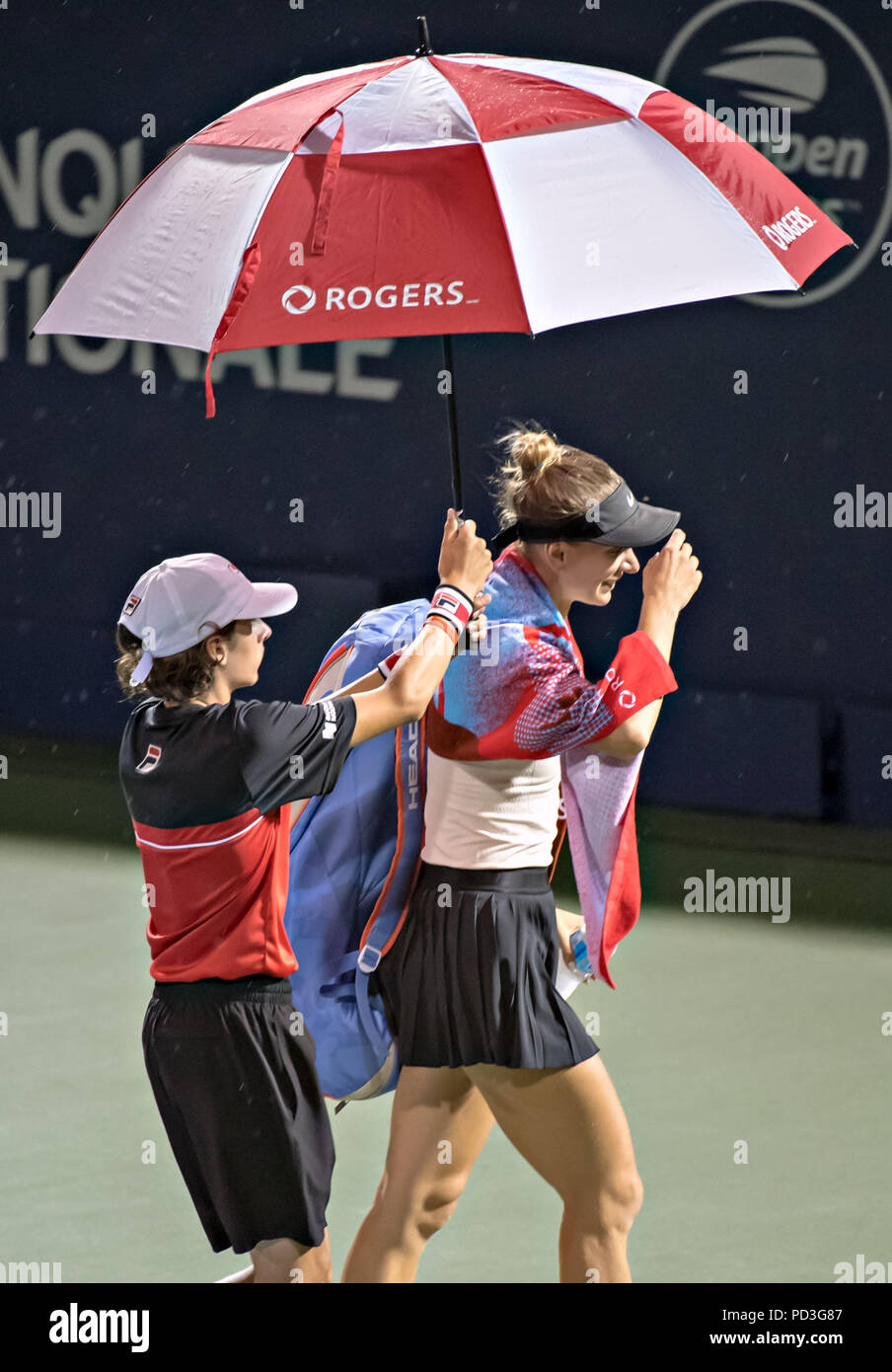 Montreal. 6th Aug, 2018. Sesil Karatantcheva (R) of Bulgaria is escorted off the main court with an umbrella during the first round of women's singles match of the 2018 Rogers Cup in Montreal, Aug. 6, 2018. Remaining competitions here on Aug. 6, 2018 have been cancelled due to rainfall. Credit: Andrew Soong/Xinhua/Alamy Live News Stock Photo