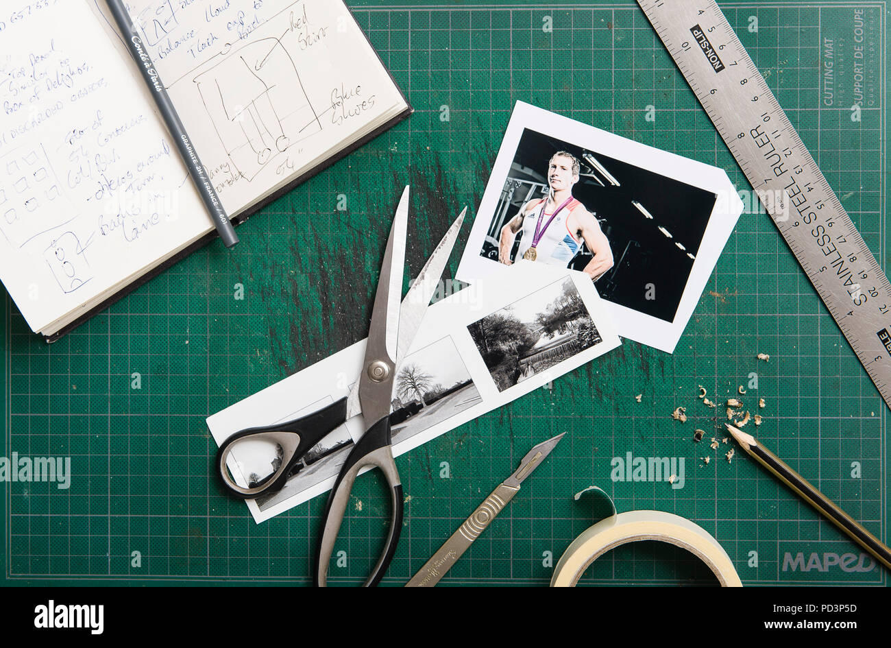 Top down view of cutting mat with sketchbook, scissors, tape, ruler, prints and pencil. Stock Photo