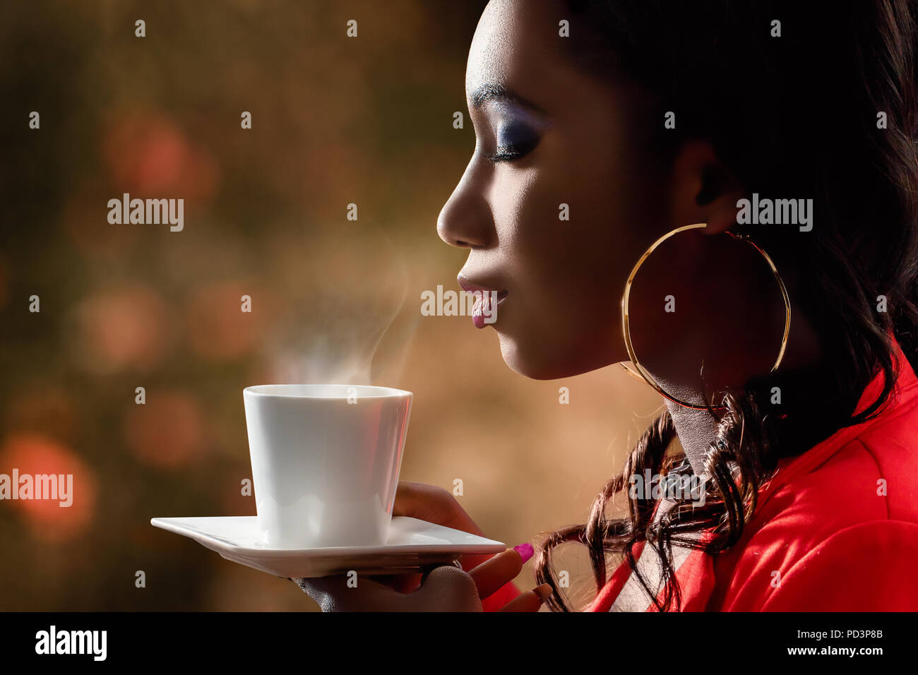 Close up side view of attractive african woman smelling scent of hot beverage.Low key portrait of woman with directional backlit ambient light holding Stock Photo