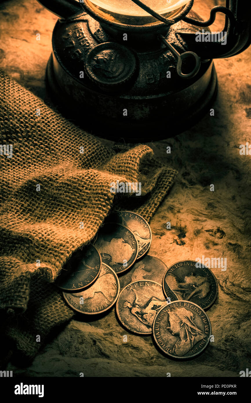 Old British penny coins illuminated by an oil lamp. Stock Photo