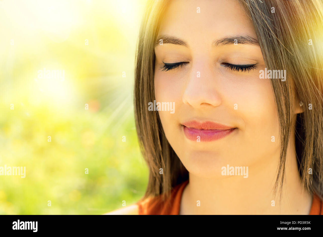 Close up portrait of attractive relaxed young woman meditating outdoors.Girl with eyes closed against bright colorful outdoor background. Stock Photo