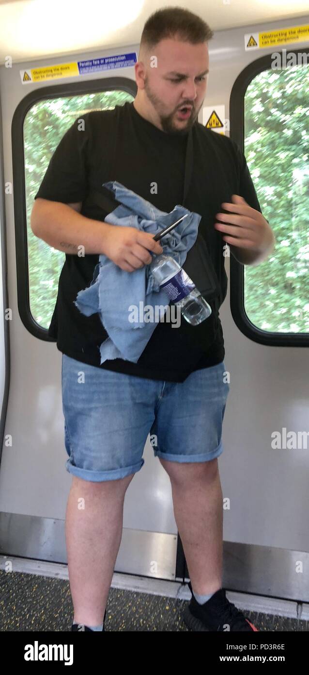 Commuter Sam Johnson felt the heat on his tube journey today - so decided to cut his jeans into a pair of denim shorts. Sam was travelling on a delayed District Line when he borrowed a pair of scissors from another traveler and began cutting away at his trousers.  Featuring: Sam Johnson Where: London, United Kingdom When: 06 Jul 2018 Credit: Rocky/WENN.com Stock Photo