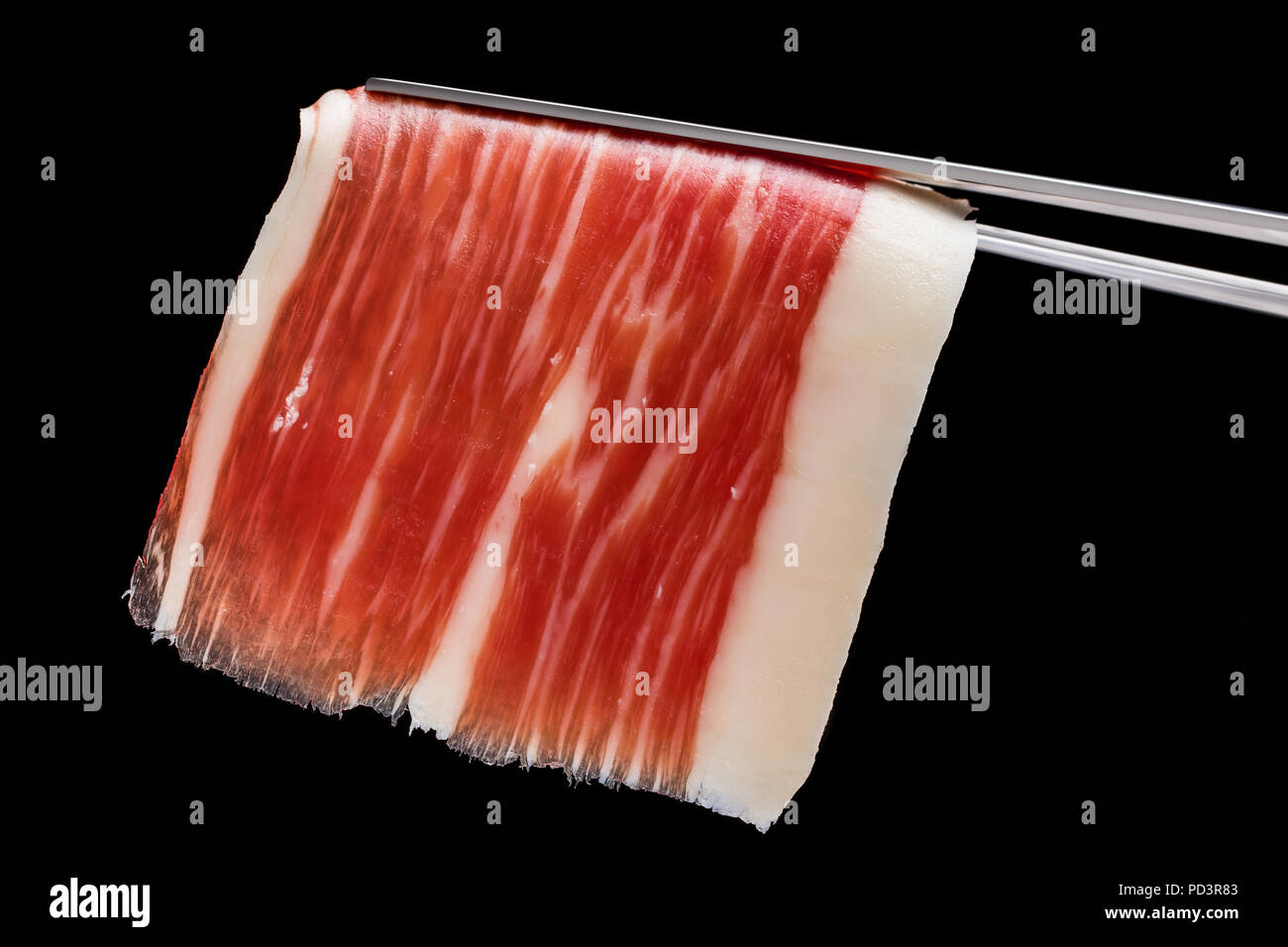 Extreme macro close up of cut piece of cured Spanish bellota pork ham on tweezer. Stock Photo
