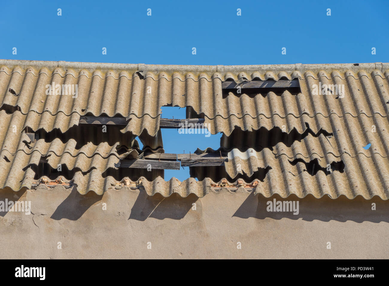 Corrugated asbestos roof in poor state of repair against a clear blue sky. Stock Photo