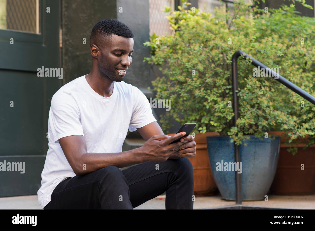 Young man using cellphone on step in streets of New York, US Stock Photo