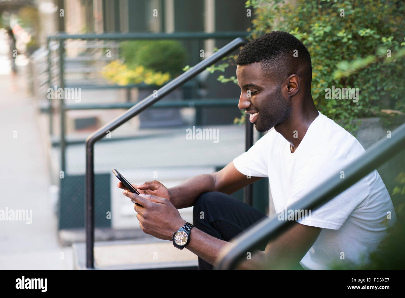 Young man using cellphone on step in streets of New York, US Stock Photo