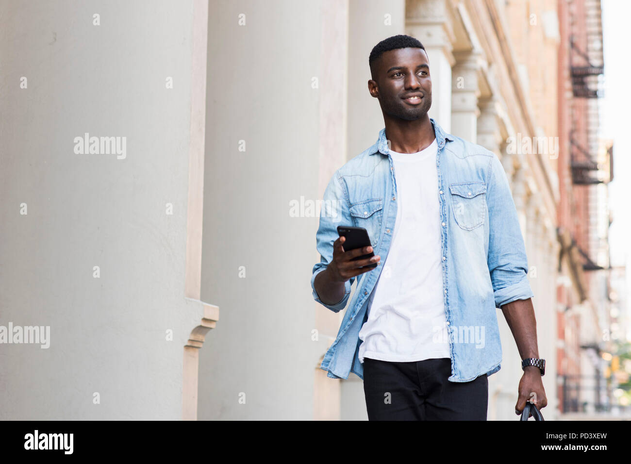 Young man with hand luggage holding cellphone in streets of New York, US Stock Photo