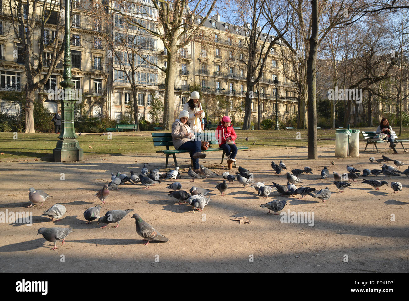 Mother and daughters feeding pigeons at a park near the Eiffel Tower in Paris Stock Photo