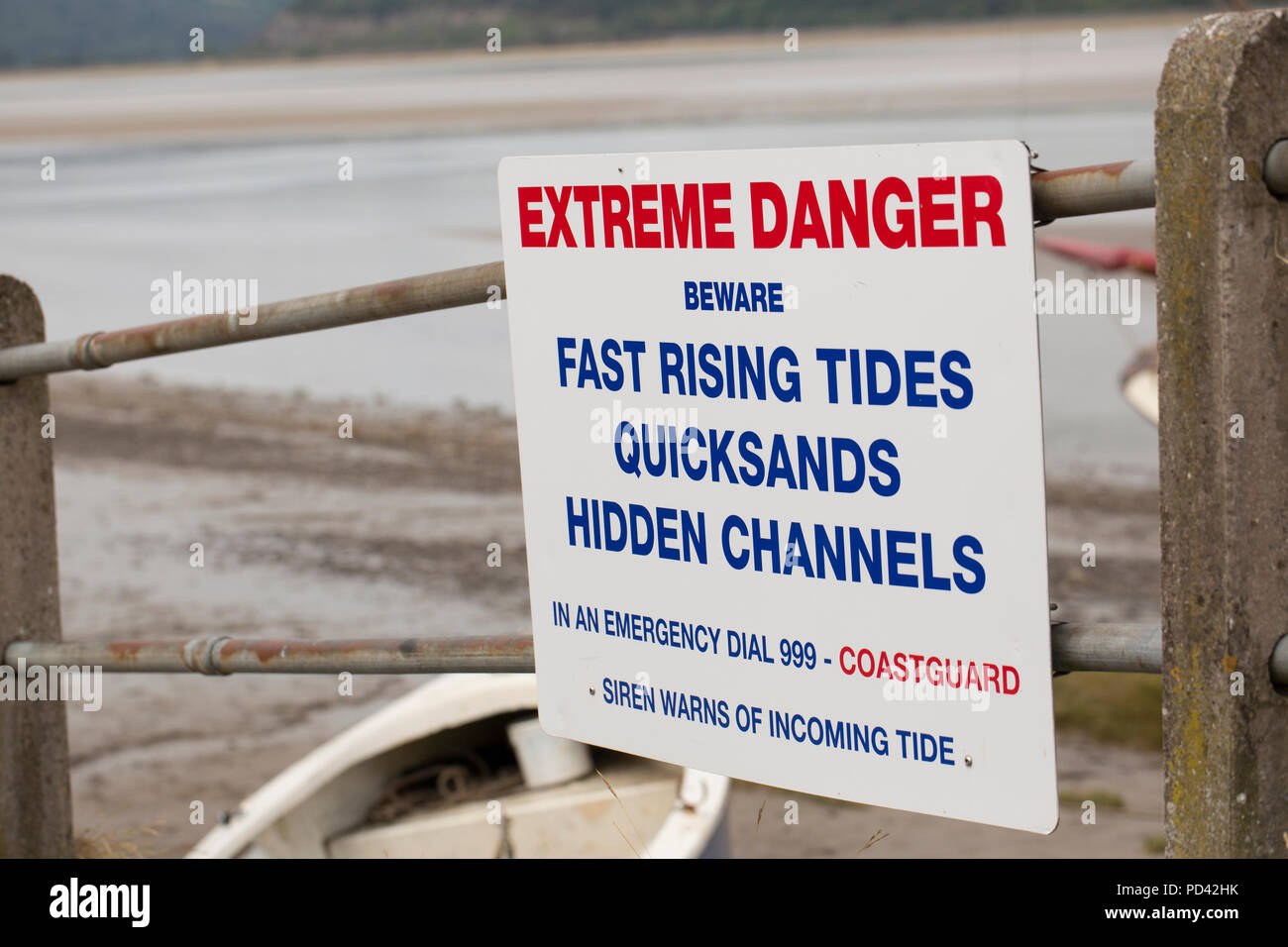A sign warning of the dangers of tides, quicksand and hidden channels on the seafront of the village of Arnside in Cumbria next to the Kent estuary. C Stock Photo