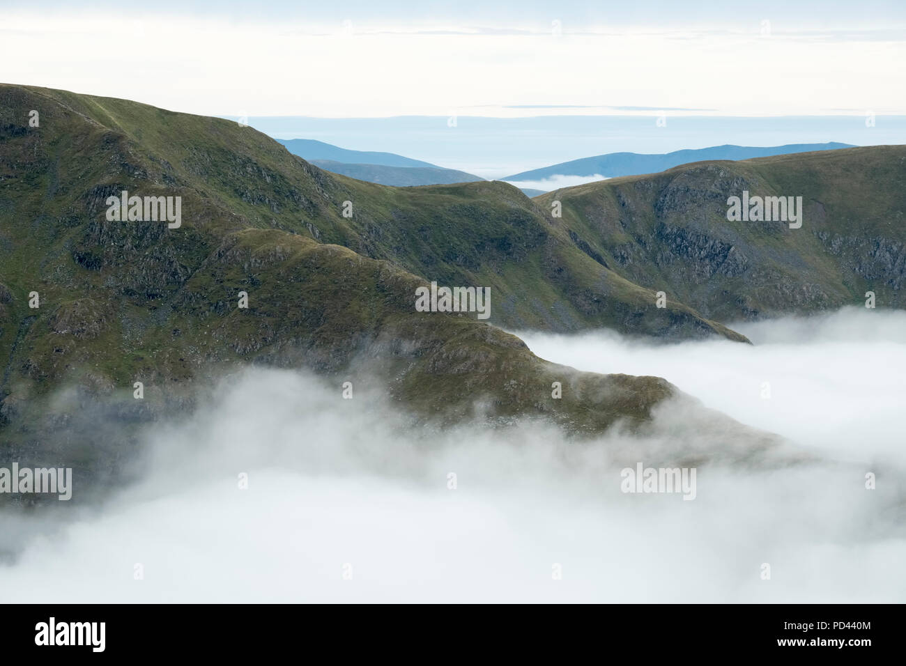 Lake District fells emerging above the clouds. A hazy summer morning in the mountains of Cumbria. Rough Crag in the foreground with High Street behind Stock Photo