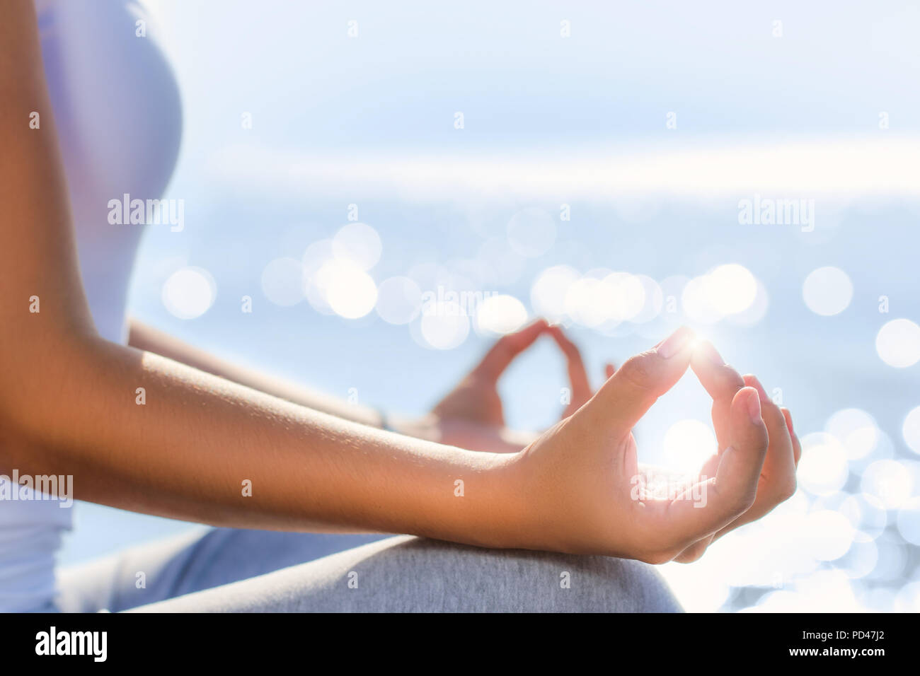 Macro close up of female hands in yoga position next to sea.Early morning sun reflection on water in background. Stock Photo
