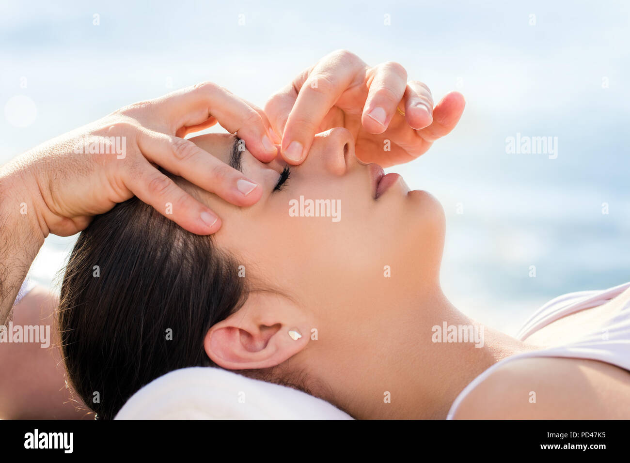 Close up of osteopath doing facial therapy on woman outdoors.Therapist applying pressure with fingers between eyes. Stock Photo