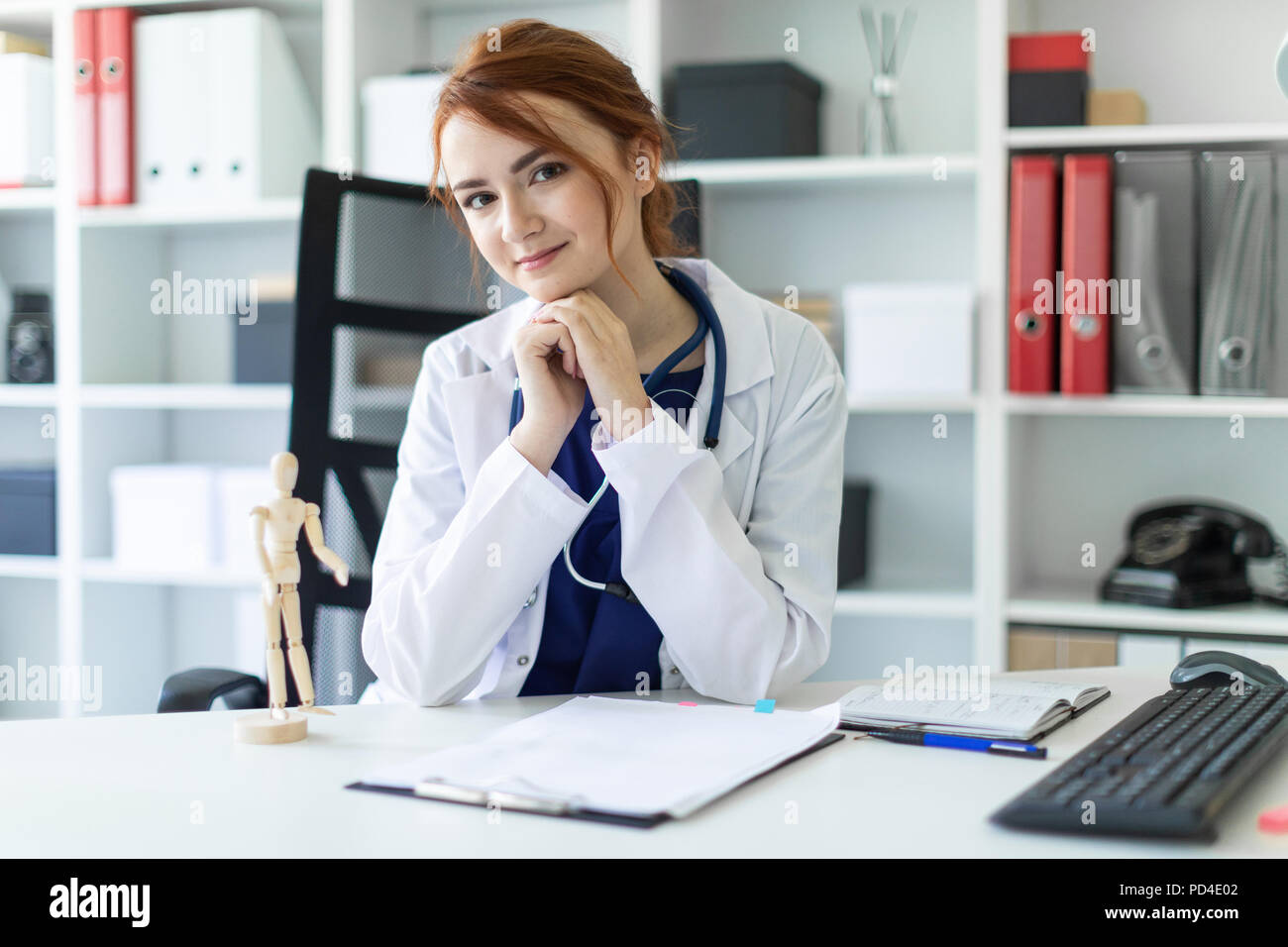 A beautiful young girl in a white robe is sitting at a table in the office. Stock Photo